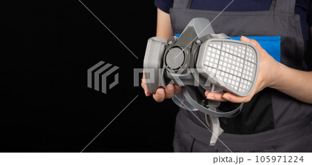 Respirator with dust and gas filters in the hands of a person on a black background. 105971224