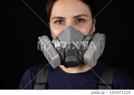 A woman wears a protective respirator with dust and gas filters on a black background. 105971226
