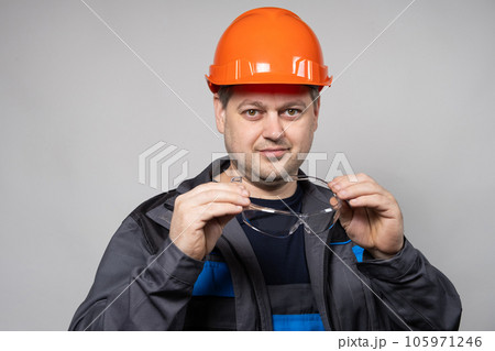 A construction worker in a helmet and overalls put on goggles protective glasses on a white background. 105971246