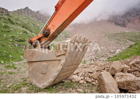 Excavator works in the highlands. Clears the consequences of a mudslide in the gorge of the mountains. repair and expansion of a road Excavator works in the highlands. Clears the consequences of a mudslide in the gorge of the mountains. repair and expansion of a road 105971432