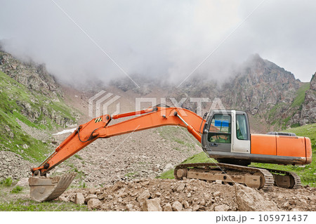 Excavator works in the highlands. Clears the consequences of a mudslide in the gorge of the mountains. repair and expansion of a road Excavator works in the highlands. Clears the consequences of a mudslide in the gorge of the mountains. repair and expansion of a road 105971437