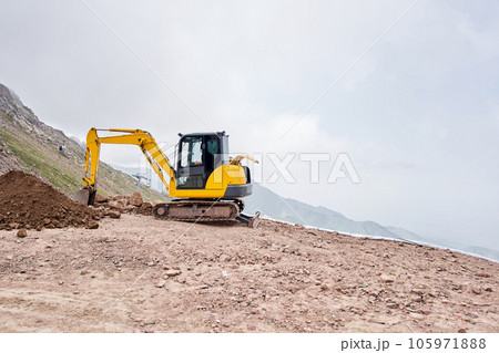 Excavator works in the highlands. Makes a trench for communications. water and electricity. in the gorge of the mountains. repair and expansion of a road 105971888