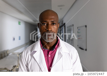Portrait of african american male doctor wearing lab coat in corridor at hospital 105972447