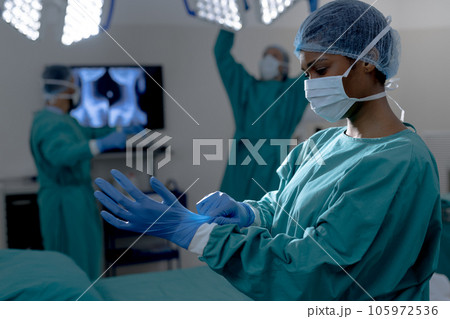 African american female surgeon wearing surgical gown and gloves in operating theatre at hospital 105972536