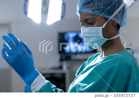 African american female surgeon wearing surgical gown and gloves in operating theatre at hospital 105972537