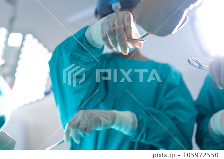 Diverse surgeons wearing surgical gowns operating on patient in operating theatre at hospital 105972550