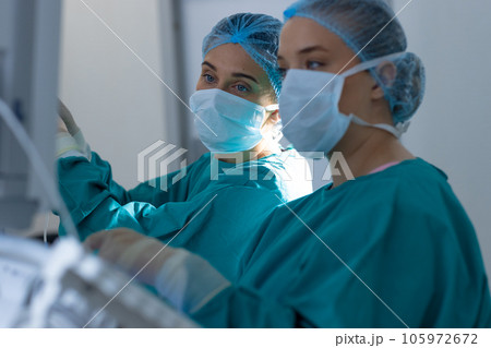 Diverse surgeons wearing surgical gowns operating on patient in operating theatre at hospital 105972672
