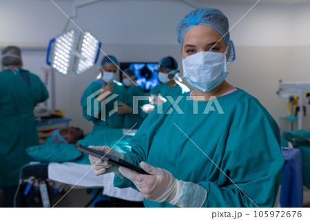 Portrait of caucasian female surgeon wearing surgical gown in operating theatre at hospital 105972676