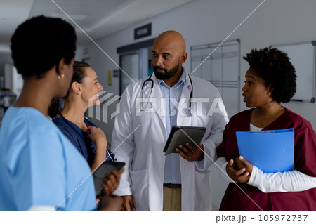 Diverse doctors using tablets and discussing work in corridor at hospital Diverse doctors using tablets and discussing work in corridor at hospital 105972737