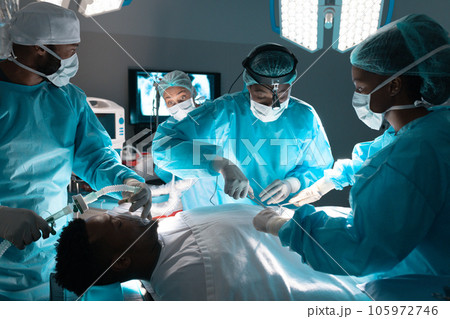 Diverse surgeons wearing surgical gowns operating on patient in operating theatre at hospital 105972746