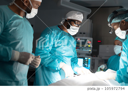 Diverse surgeons wearing surgical gowns operating on patient in operating theatre at hospital 105972794