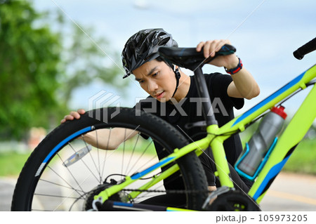Concentrated male cyclist checking tire or transmission system of his mountain bike. 105973205