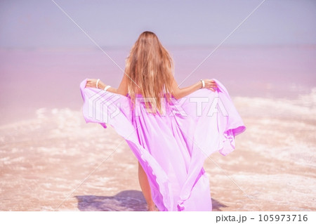 Woman pink salt lake. Against the backdrop of a pink salt lake, a woman in a long pink dress takes a leisurely stroll along the white, salty shore, capturing a wanderlust moment. Woman pink salt lake. Against the backdrop of a pink salt lake, a woman in a long pink dress takes a leisurely stroll along the white, salty shore, capturing a wanderlust moment. 105973716