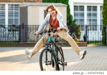 Funny girl riding a bike in the evening in a calm city. Young girl joking and having fun. Eco-friendly urban transport. 105974362