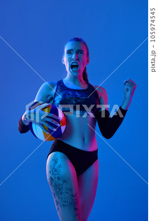 Motivation to win. Emotional woman, volleyball player shouting to cheer up before game against blue studio background in neon light Motivation to win. Emotional woman, volleyball player shouting to cheer up before game against blue studio background in neon light 105974545