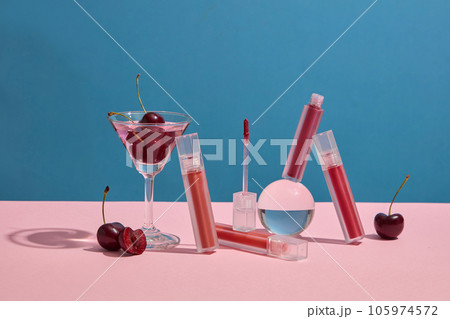 Concept for advertising lipstick with cherry concept. Lipsticks mockup decorated with cherries and glass cup on blue background. Cherries contain vitamin C and vitamin B, which help keep lips supple Concept for advertising lipstick with cherry concept. Lipsticks mockup decorated with cherries and glass cup on blue background. Cherries contain vitamin C and vitamin B, which help keep lips supple 105974572