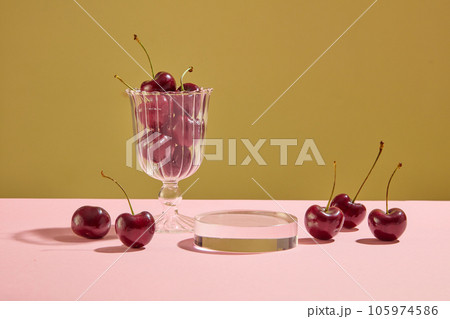 Background for the presentation of cosmetic products with ingredient from cherry. A transparent podium with ripe cherries and glass cup decorated on brown and pink background Background for the presentation of cosmetic products with ingredient from cherry. A transparent podium with ripe cherries and glass cup decorated on brown and pink background 105974586