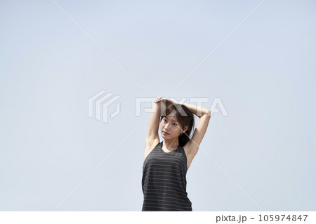 young asian woman in sportswear stretching arms outdoors against blue sky young asian woman in sportswear stretching arms outdoors against blue sky 105974847