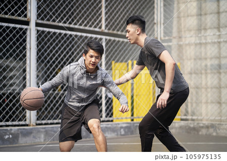 two young asian adult men playing one-on-one basketball on outdoor court two young asian adult men playing one-on-one basketball on outdoor court 105975135