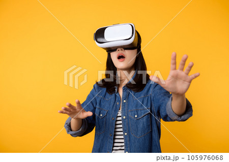 Young asian woman get experienced wearing virtual reality headset game entertainment isolated on yellow background. Winner of cyber future video game concept. 105976068