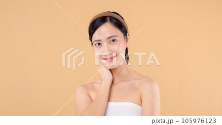 Beautiful girl asian model touching fresh glowing hydrated facial skin on beige background closeup. Beauty face young woman with natural makeup and healthy skin portrait. Skin care concept 105976123