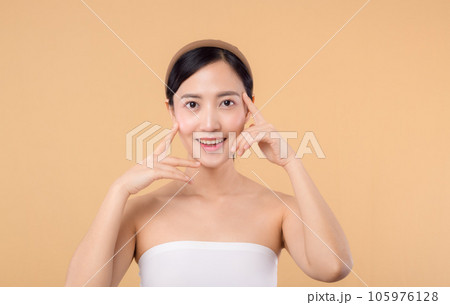 Beautiful girl asian model touching fresh glowing hydrated facial skin on beige background closeup. Beauty face young woman with natural makeup and healthy skin portrait. Skin care concept 105976128