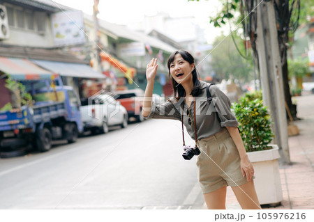 Smiling young Asian woman traveler hitchhiking on a road in the city. Life is a journey concept. Smiling young Asian woman traveler hitchhiking on a road in the city. Life is a journey concept. 105976216