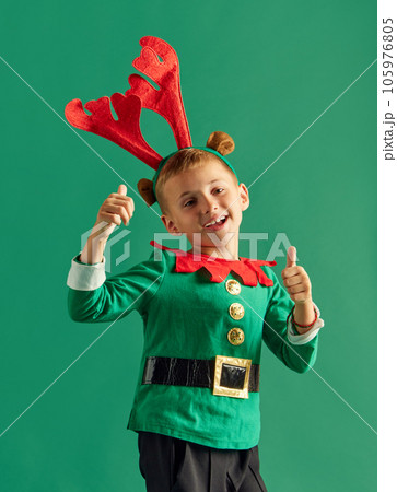 Portrait fo little boy, happy child in costume of elf cheerfully posing against green studio background 105976805