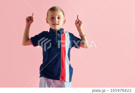Little child, boy in sport style clothes raising fingers up, playing against pink studio background 105976822