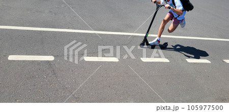 The scooter rides along the track with markings for bicycles, legs are visible. The scooter rides along the track with markings for bicycles, legs are visible. 105977500