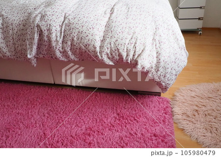 Cozy compact bedroom, white furniture, pink carpet and tulle curtains. Fluffy feather blanket thrown over the double bed. Romantic morning. Light from the window. The blanket hangs down to the floor Cozy compact bedroom, white furniture, pink carpet and tulle curtains. Fluffy feather blanket thrown over the double bed. Romantic morning. Light from the window. The blanket hangs down to the floor 105980479