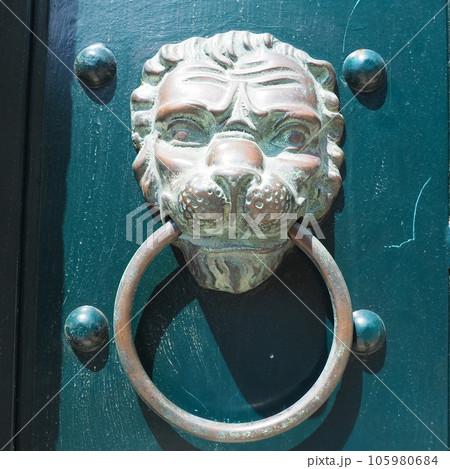 A door knocker is a fixture on the front door of a house. It is made of metal and has the form of a ring, which is knocked on the metal part of the door knocker fixed to the wall. Muzzle of a lion 105980684