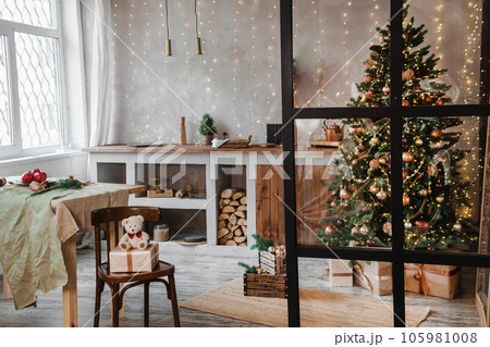Home New Year's interior. Christmas tree with gifts, decorated with garlands in the kitchen. Cozy atmosphere of a home holiday, loft design of the room, Scandinavian style. Home New Year's interior. Christmas tree with gifts, decorated with garlands in the kitchen. Cozy atmosphere of a home holiday, loft design of the room, Scandinavian style. 105981008