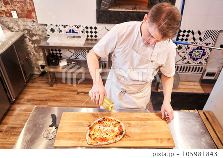 Closeup hand of chef baker in uniform blue apron cutting pizza at kitchen Closeup hand of chef baker in uniform blue apron cutting pizza at kitchen 105981843