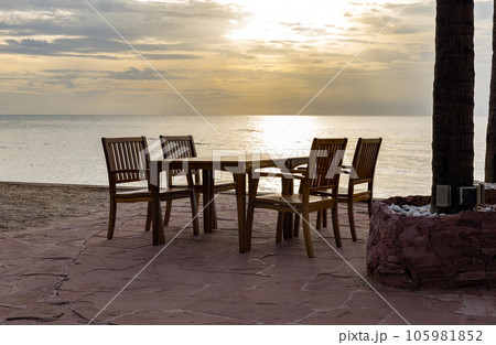 dining table sea view on sand beach with sunset, wood chairs and table dining table sea view on sand beach with sunset, wood chairs and table 105981852
