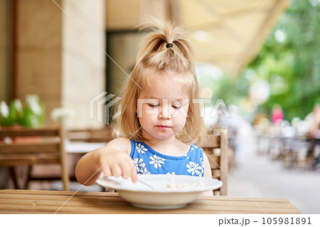Little kid having breakfast at cafe. Adorable girl drinking still water, eating rice porridge with mango. enjoying breakfast.  105981891