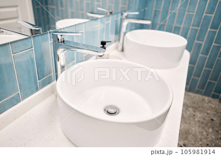 Two sinks in the bathroom sink next to stylish decorations. A beautiful sink with a metal faucet next to an mirror and a shelf with hand towels.. Two sinks in the bathroom sink next to stylish decorations. A beautiful sink with a metal faucet next to an mirror and a shelf with hand towels.. 105981914