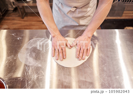 The chef prepare pizza. Raw pizza ready to bake. Cook in a apron in the kitchen Rolls out pizza dough. boxes for food delivery on background. The chef prepare pizza. Raw pizza ready to bake. Cook in a apron in the kitchen Rolls out pizza dough. boxes for food delivery on background. 105982043