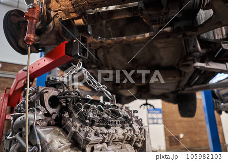 A car mechanic inspects the engine with a flashlight. Engine Block on a repair stand with Special crane jack. Technical service station for car. A car mechanic inspects the engine with a flashlight. Engine Block on a repair stand with Special crane jack. Technical service station for car. 105982103