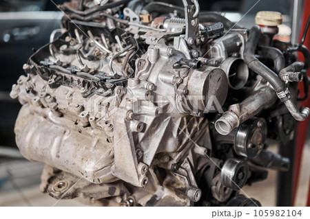 A car mechanic inspects the engine with a flashlight. Engine Block on a repair stand with Special crane jack. Technical service station for car. 105982104