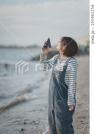 オーバーオールを着た女性が拾ったおもちゃのピストルを持って空を見上げてる オーバーオールを着た女性が拾ったおもちゃのピストルを持って空を見上げてる 105982256