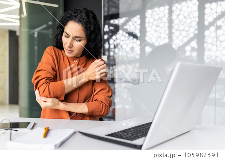 Businesswoman at the workplace sits tired and overworked, has severe pain in her hands and elbow joints. Businesswoman at the workplace sits tired and overworked, has severe pain in her hands and elbow joints. 105982391