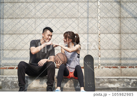 young asian adult man and woman bumping fists on a outdoor basketball court 105982985