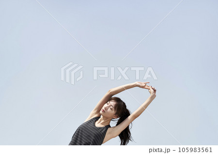young asian woman in sportswear stretching arms outdoors against blue sky 105983561