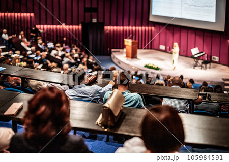 Business and entrepreneurship symposium. Female speaker giving a talk at business meeting. Audience in conference hall. Rear view of unrecognized participant in audience. Business and entrepreneurship symposium. Female speaker giving a talk at business meeting. Audience in conference hall. Rear view of unrecognized participant in audience. 105984591