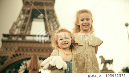 Two smiling little sisters hug each other and pose at the famous Eiffel Tower. Paris, France 105985575