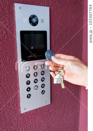 A young woman types the apartment code on the electronic intercom panel, opens the door with a sensor key. Protection and security concept. A young woman types the apartment code on the electronic intercom panel, opens the door with a sensor key. Protection and security concept. 105987764