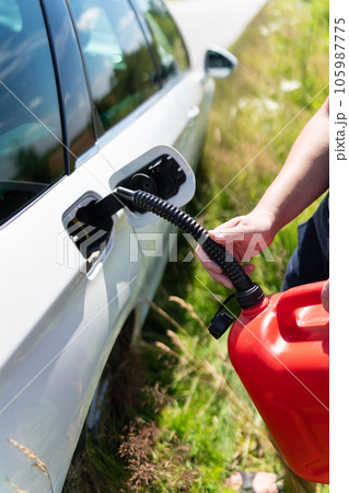 The driver fills up the empty tank of the car from a red canister on the side of the road. Close-up, vertical photo. The driver fills up the empty tank of the car from a red canister on the side of the road. Close-up, vertical photo. 105987775
