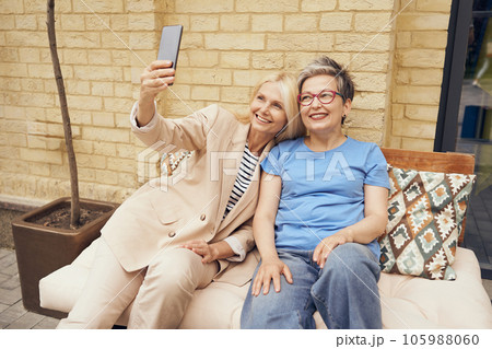 Mature smiling women friends taking selfie on phone while sitting in cafe terrace 105988060