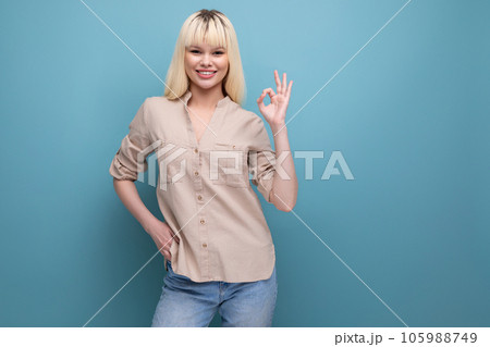 cheerful blond young woman in shirt on studio blue background 105988749